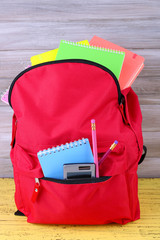 Red bag with school equipment on wooden background