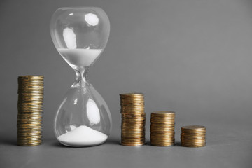 Hourglass with coins on gray background