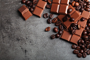 Milk chocolate pieces and coffee grains on gray background