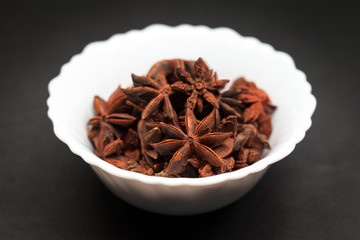 Organic Star anise or Chakra Phool (Illicium verum) in white ceramic bowl on dark background.