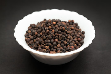 Organic Black pepper (Piper nigrum) in white ceramic bowl on dark background.