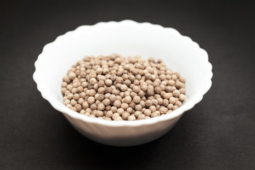 Organic White Pepper (Piper nigrum) in white ceramic bowl on dark background.