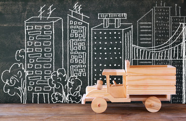 photo of wooden toy truck in front of chaklboard with city illustration. 