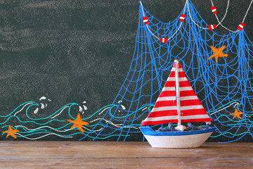 photo of wooden sailing boat in front of chaklboard with nautical illustrations.  © tomertu