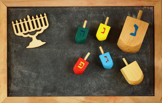 image of jewish holiday Hanukkah with menorah (traditional Candelabra) and wooden colorful dreidels (spinning top) over chalkboard background
