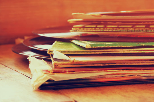 selective focus image of records stack with record on top over wooden table. vintage filtered
