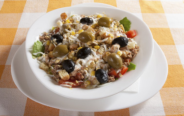 Delicious tuna salad with lettuce, tomato, egg, cucumber, olives, served in a white bowl.