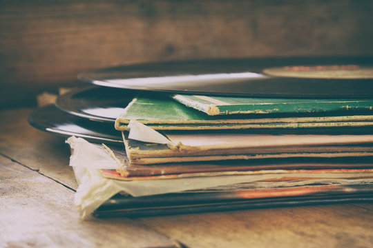 selective focus image of records stack with record on top over wooden table. vintage filtered
