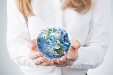 Close-up of blonde's hands who holds the globe with western hemisphere. A woman dressed in formal clothes. A light grey background. Elements of this image furnished by NASA.
