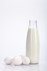 Glass bottle of milk and some eggs. White background