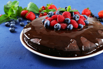 Delicious chocolate cake with summer berries on blue tablecloth, closeup