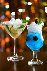 Glasses of cocktails with ice on blurred lights background
