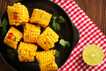 Tasty grilled corn and vegetables on black crockery decorated with plaid pattern cotton serviette
