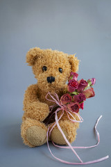 Brown teddy bear holding rose paper flower bouquet