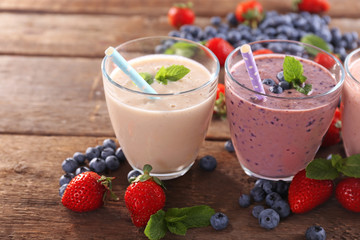 Tasty blueberry, strawberry and milk yogurts in a row decorated with berries and mint on wooden background, close up