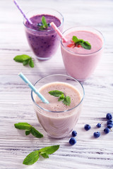 Fresh strawberry, blueberry and milk yogurts with mint and berries around on light wooden background