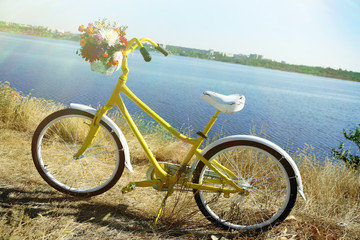 Fototapeta premium Beautiful yellow bicycle with bouquet of flowers in basket, outdoors