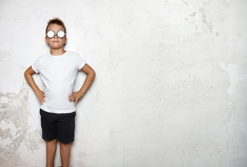 Boy wearing white tshirt, shorts stands on a wall background of