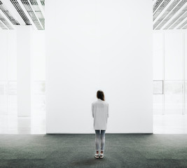 Young woman walking through a gallery and looking at the canvas
