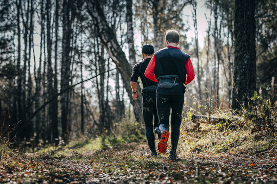 Two Men Runner Running In Autumn Forest During Mountain Marathon. View From Back