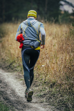 Male Runner Running Through Forest Road Behind Him With A Water Bottle. View From Back