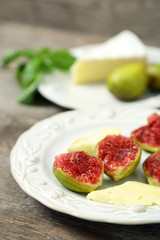 Ripe figs and cheese on plate, on wooden background