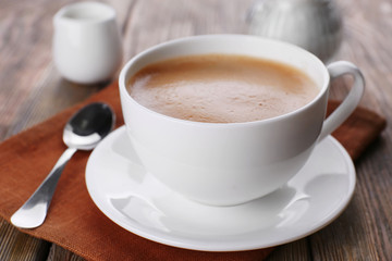 Cup of coffee with cream on brown napkin closeup