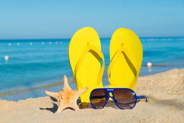 Fototapeta na wymiar Sunny positive beach vacation. Yellow sandals, sunglasses and starfish on a background of the sea