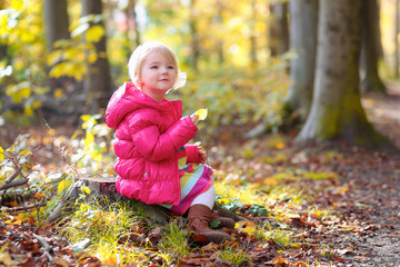 Cute little girl wearing warm pink jacket playing in beautiful autumn forest on sunny fall day