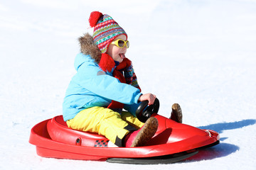 Fototapeta na wymiar Happy child enjoying winter vacation in Alpine resort in Austria. Little girl playing in the snow. Active sportive toddler riding sledge.
