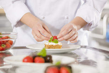 Obraz na płótnie Canvas Chef decorates dessert cake with strawberry
