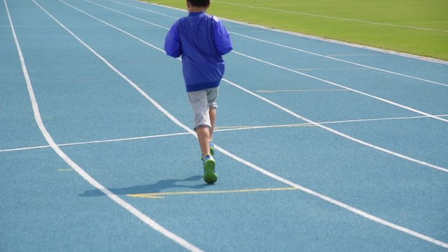 Young Asian boy running on blue track in the stadium in day time to practice himself