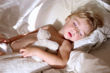 Sweet little child sleeping in bed. Healthy kid, blonde toddler girl, resting in bed in white sunny bedroom. © cromary