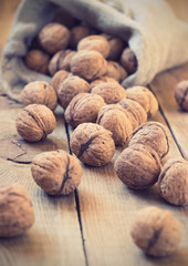 Pile of walnuts in shell inbag on a wooden background