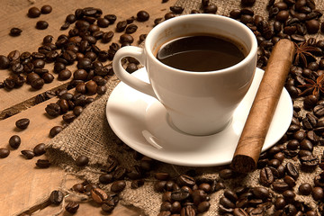 Coffee cup with coffee beans, cigar, cinnamon  on bagging on wood.