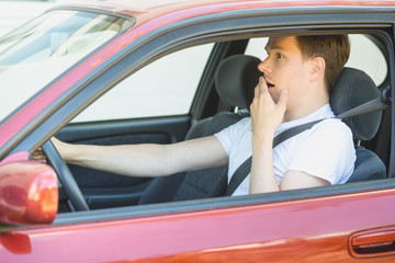 Junger Mann sitzt im Auto und ist schockiert