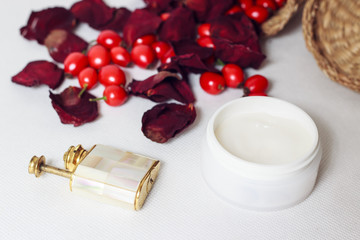 Cream, old flacon, creel, petals of rose and rose hips on white background