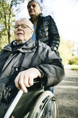 Obraz premium Seniorin schiebt ihren Mann im Rollstuhl durch einen Park