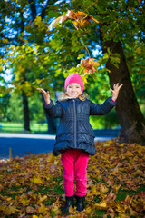 cheerful little girl playing with maple leaves in autumn park