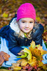 beautiful little girl with maple leaves lying in autumn park