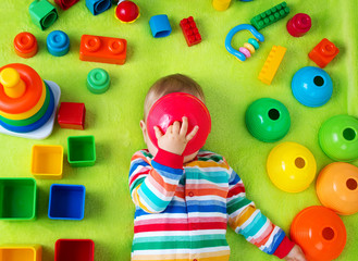 Baby boy lying on the blanket with many toys around
