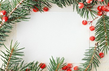 Blank white paper card framed with natural fir tree branches decor and bright red berries, wintry New Year congratulation message. 