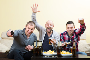 Three men watching football with beer indoor