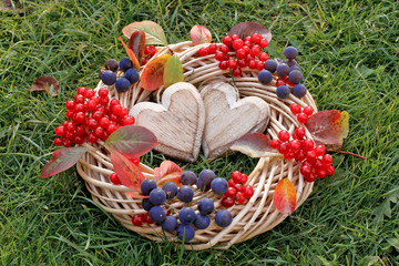 Wicker wreath with viburnum, grapes and hearts  on green grass.