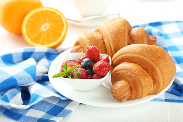 Fresh tasty croissants with berries on white wooden background