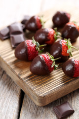 Fresh strawberries dipped in dark chocolate on grey wooden backg