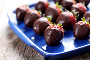 Fresh strawberries dipped in dark chocolate on grey wooden backg