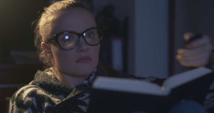 Young Woman Wearing Eye Glasses Reading A Book In The Evening. Young Woman Turning Off Tv While Reading A Book.