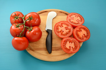 Cutting vine tomatoes with knife on wooden board