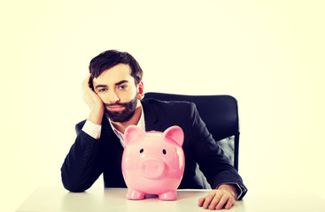 Businessman with piggybank by a desk.